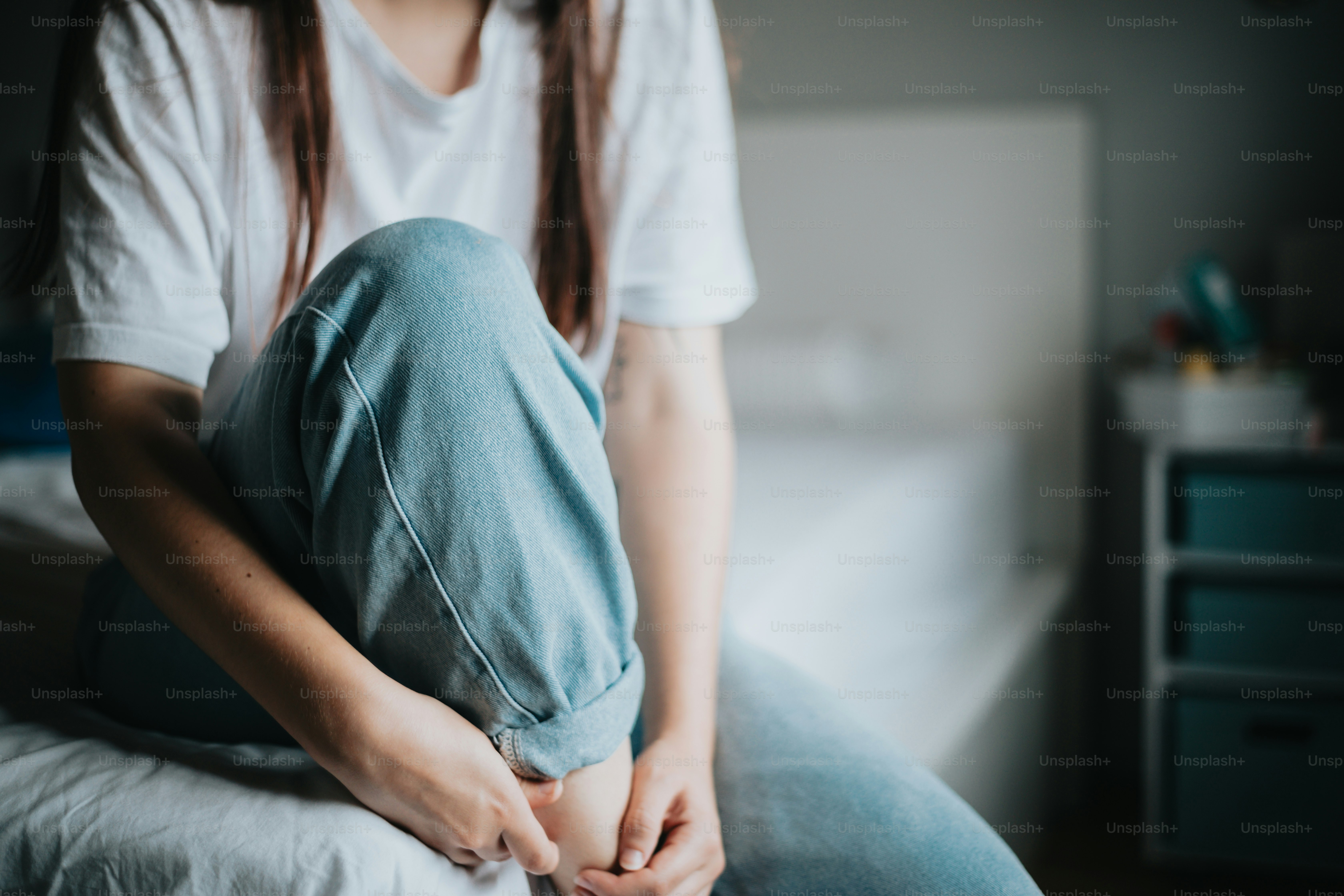 A woman sitting on a bed with her head in her hands photo – Anxious ...