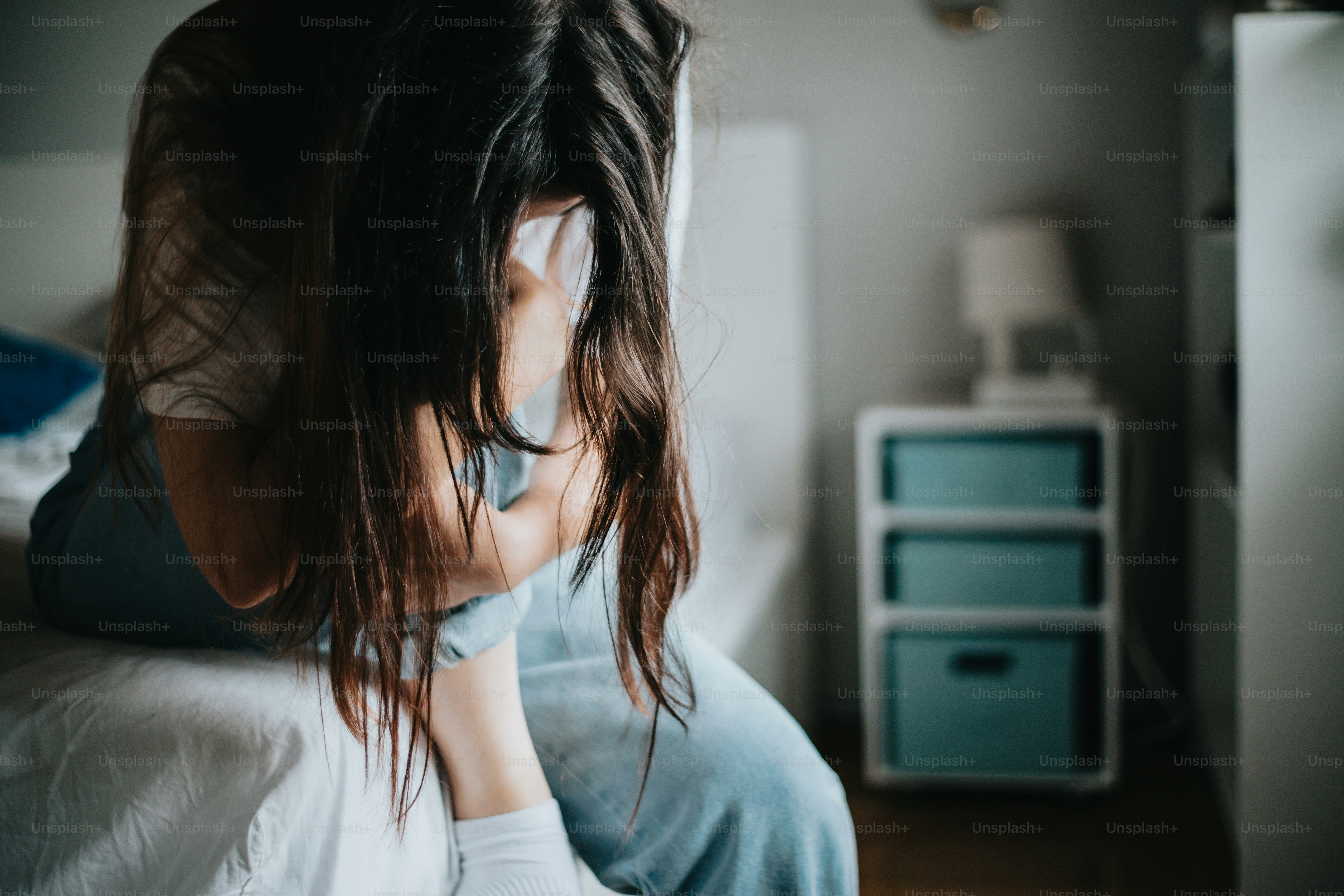 A woman sitting on a bed with her head in her hands photo – Feeling ...
