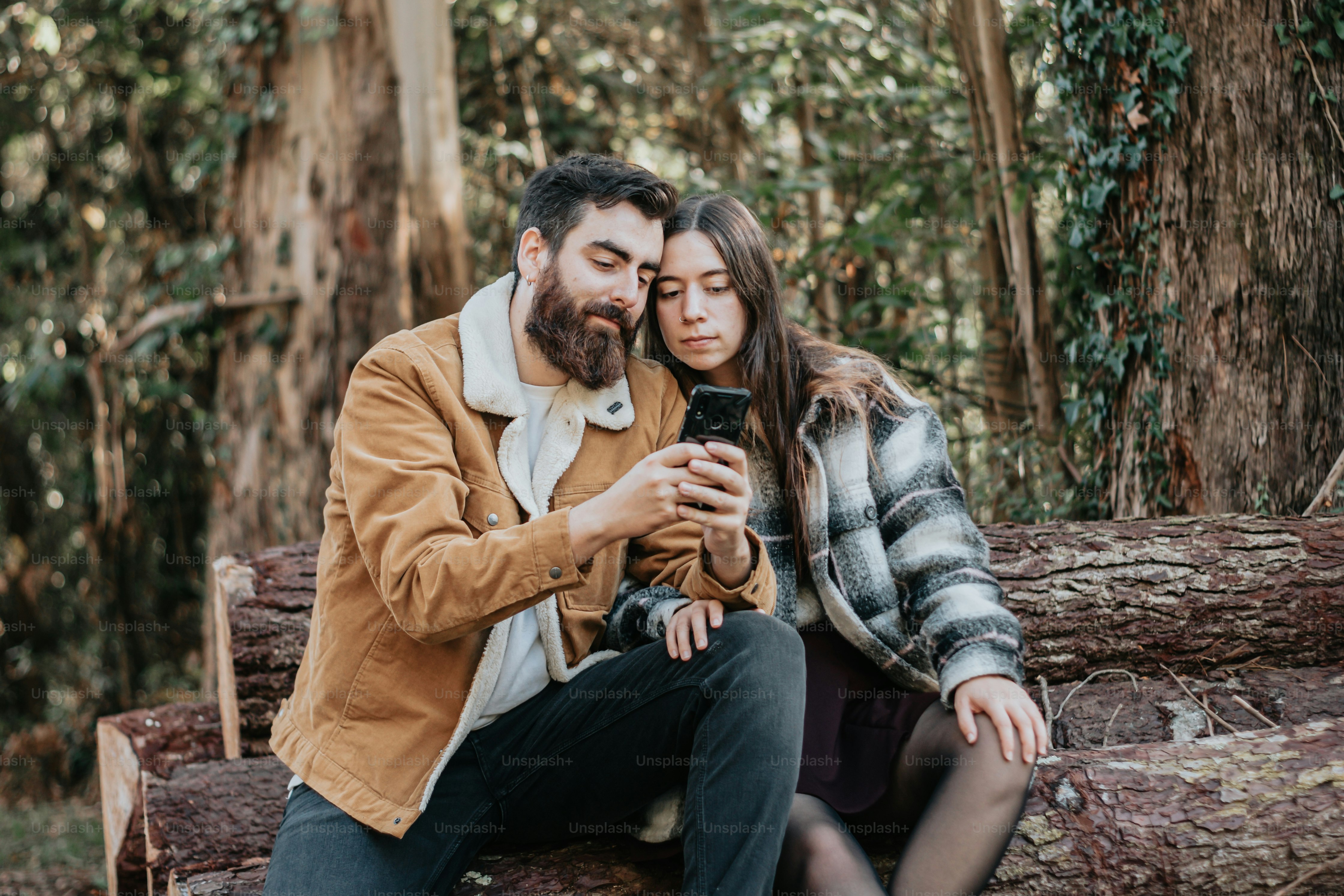 a man and woman sitting on a log in the woods