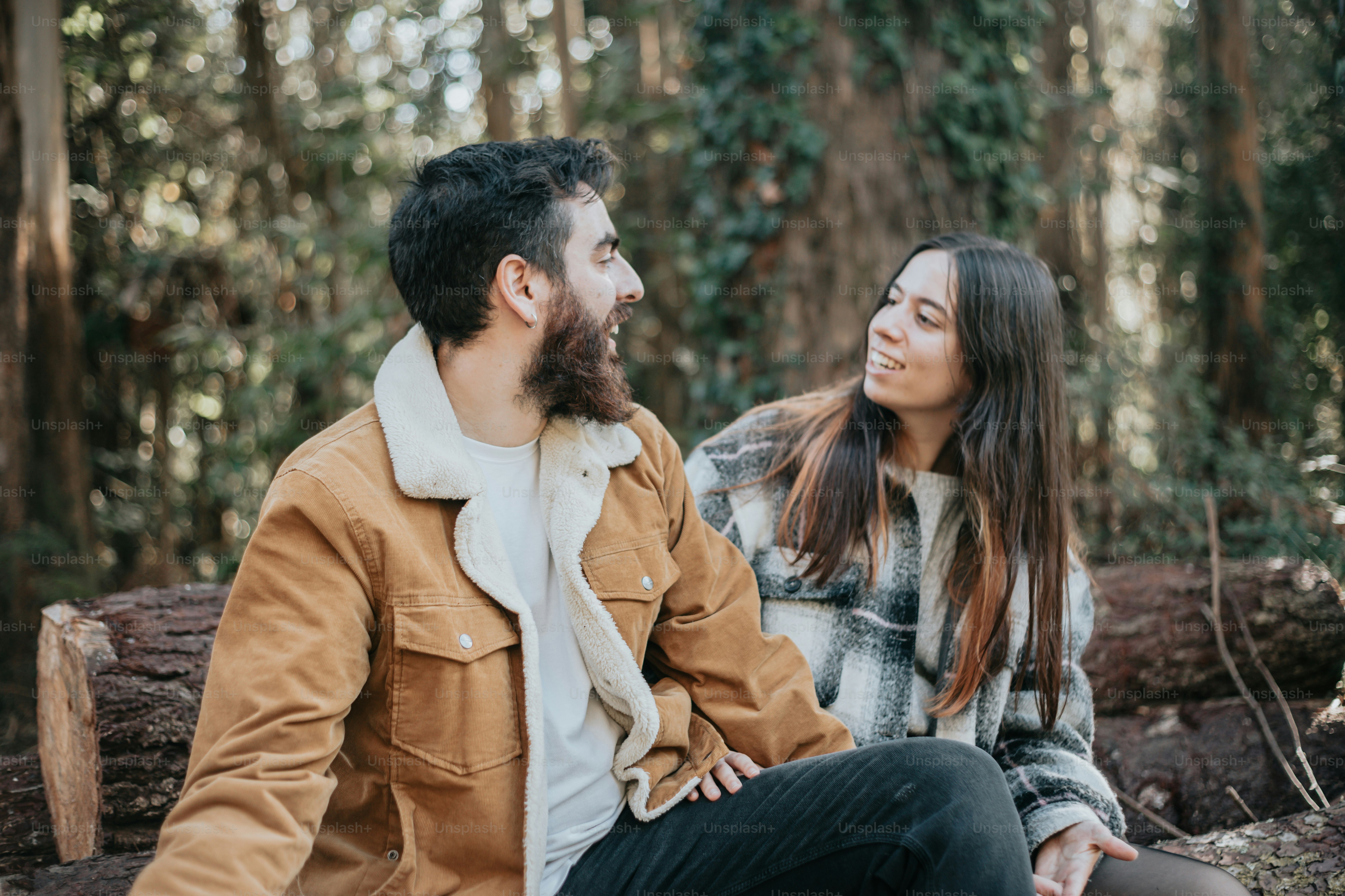 a man and woman sitting on a log in the woods
