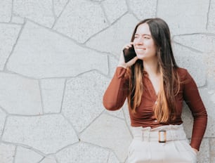 a woman talking on a cell phone next to a stone wall