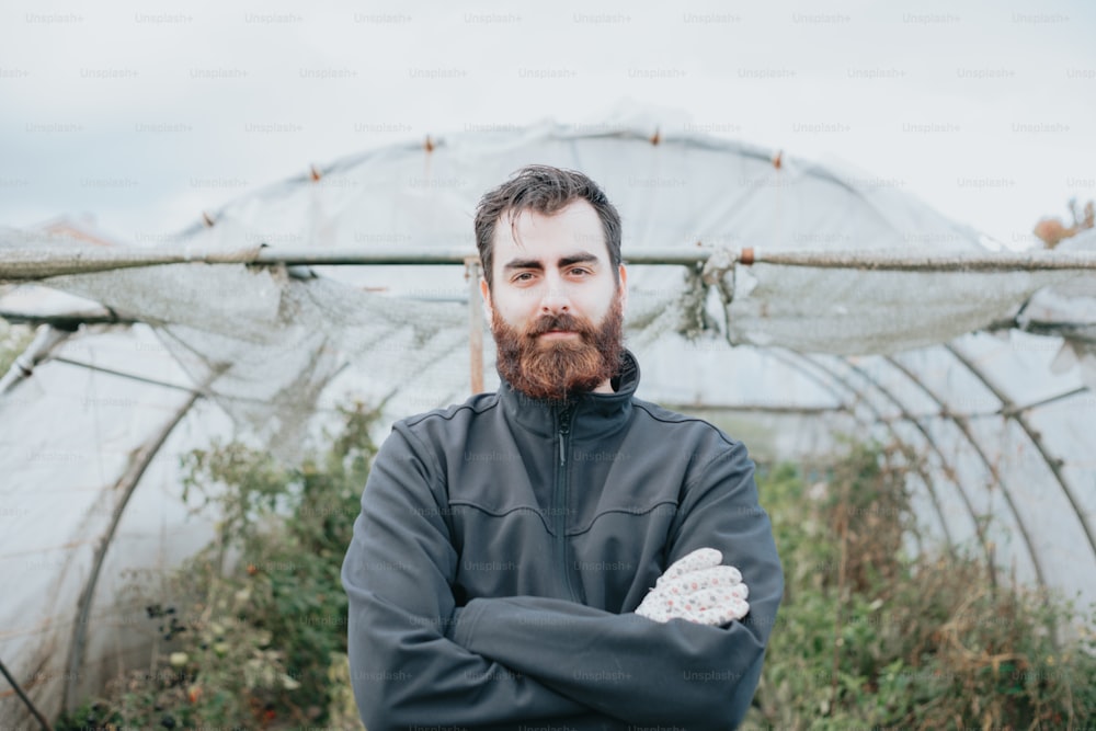 a man with a beard standing in front of a greenhouse