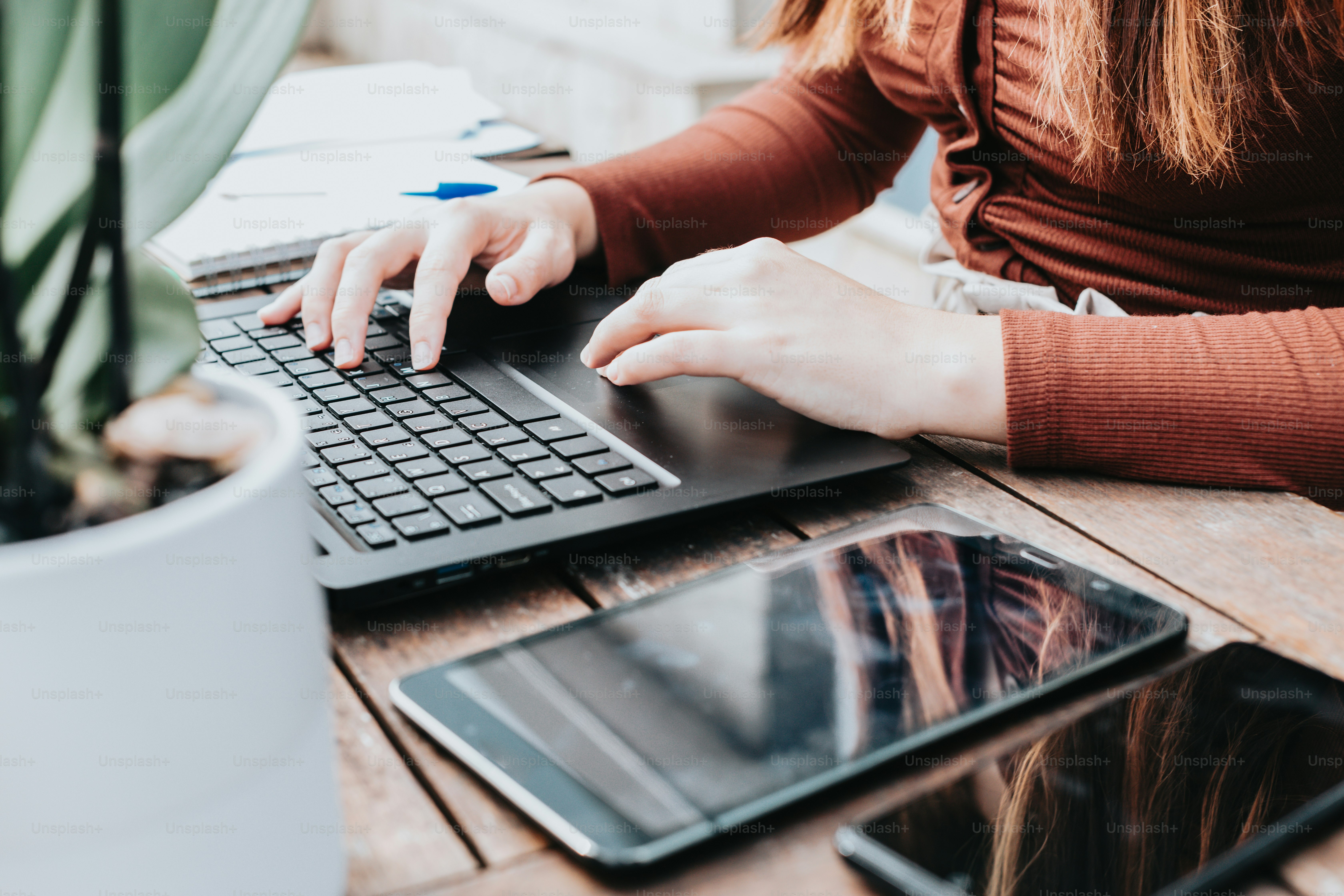 uma mulher digitando em um laptop em uma mesa de madeira