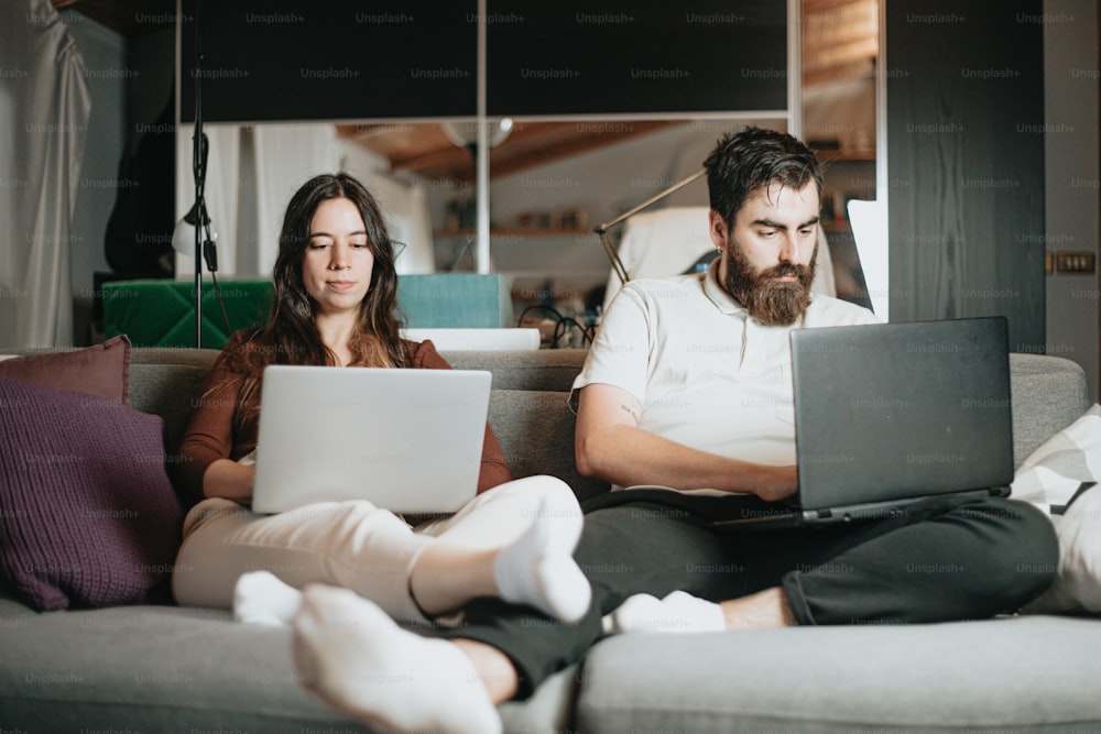 a man and a woman sitting on a couch using laptops