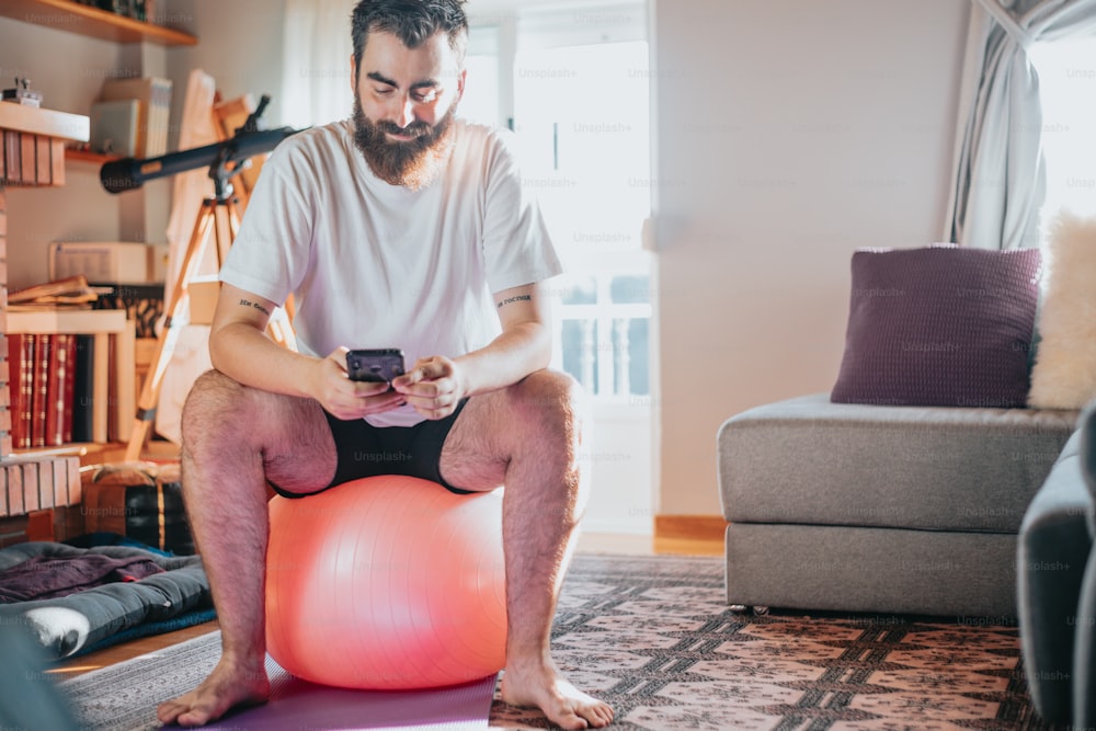 um homem sentado em uma bola de exercício olhando para seu celular