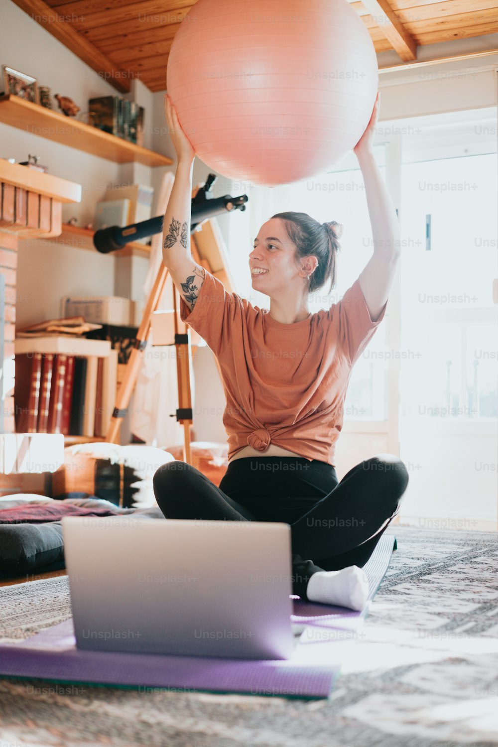 a woman sitting on a yoga mat holding a ball above her head