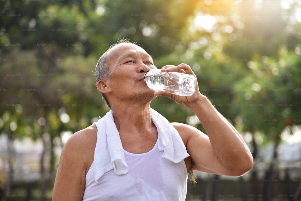 Asian senior male drinking water after exercise at park outdoor background.