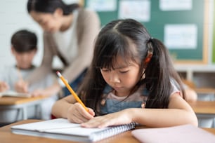 Petite écolière concentrée en train d’étudier dans la salle de classe de l’école primaire internationale.