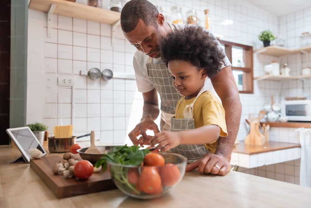 Pequeño niño afroamericano y su padre cocinando juntos en la cocina de su casa