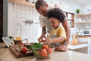 Pequeño niño afroamericano y su padre cocinando juntos en la cocina de su casa