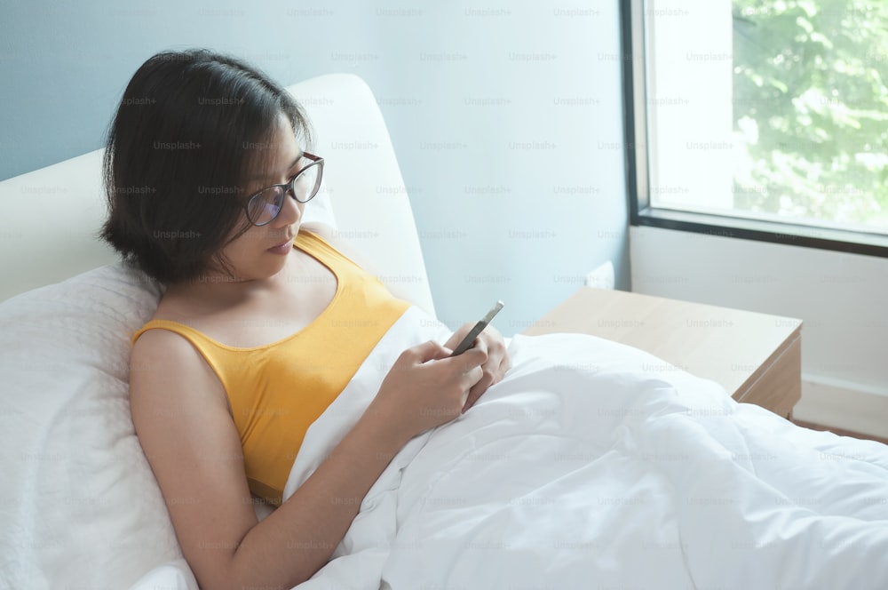 Rilassato di giovane donna asiatica sdraiata con smartphone sul letto.