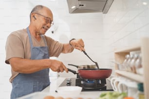 Glücklicher pensionierter asiatischer reifer Erwachsener männlicher Kochgemüse in der Pfanne in der Küche, Gesundes Essen, Essen zubereiten