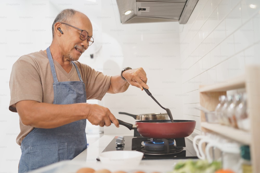 Felice pensionato Asiatico Maturo Adulto maschio che cucina verdure in padella in cucina, Cibo sano, Preparare il cibo