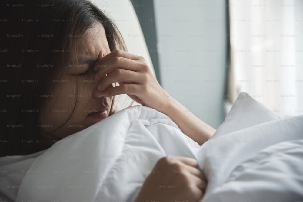 Asiatische Frau mit einer Erkältung. Mädchen mit Migräne auf ihrem Bett. Krankheit, Krankheitskonzept.