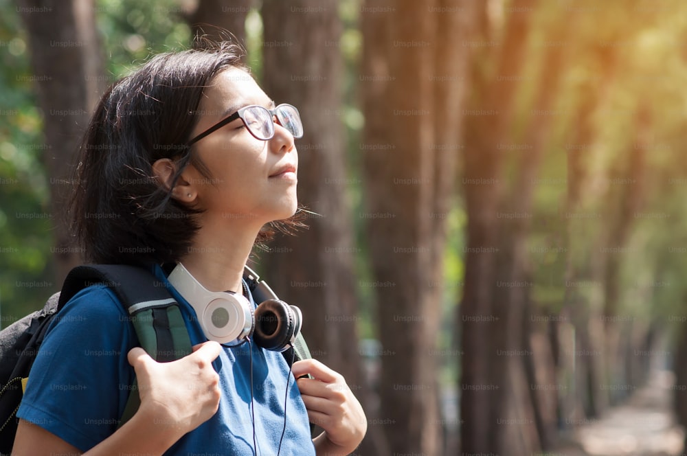 Asiatische Brille Frau Wanderin mit Rucksack atmen Natur frische Luft. Schönes Mädchen mit Kopfhörer lächelt auf Naturhintergrund.