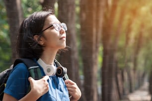 Escursionista donna con occhiali asiatici con zaino che respira aria fresca della natura. Bella ragazza con la cuffia che sorride sullo sfondo della natura.