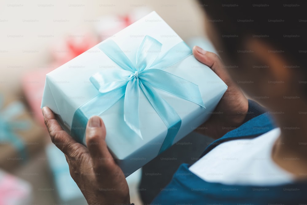 Una mujer mayor con suéter sostiene una caja de regalo azul para Año Nuevo, Cumpleaños y Navidad.