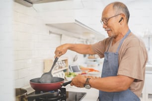 Glücklicher pensionierter asiatischer Senior, der in der Küche kocht, gesundes Essen. Gesunder Lebensstil, Essen zubereiten, Diätkonzept