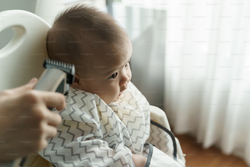 Asian little Baby boy is cutting hair by his mother with hair clipper at home.