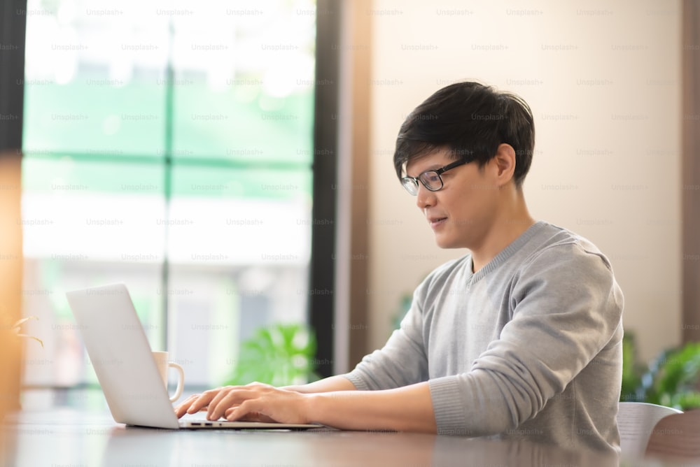 Junger asiatischer Mann mit Laptop, männlicher Freelancer arbeitet.