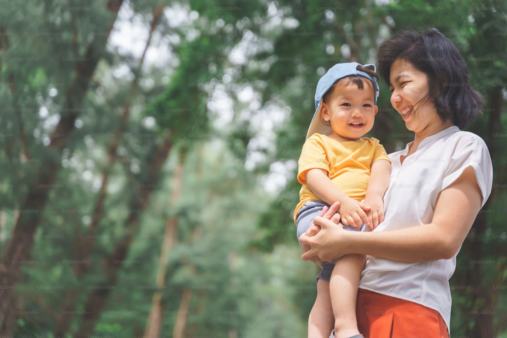 Porträt der glücklichen asiatischen jungen Mutter mit entzückendem kleinen Sohn, der in der Natur im Freien lächelt.