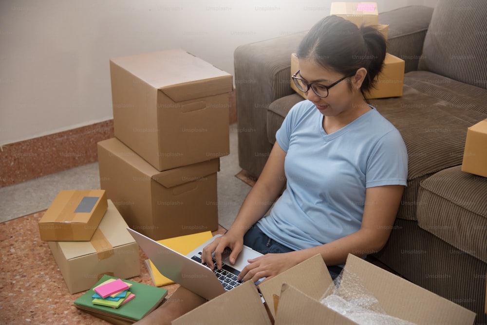 Young Asian woman looking to order details on a laptop in her small warehouse. Own business