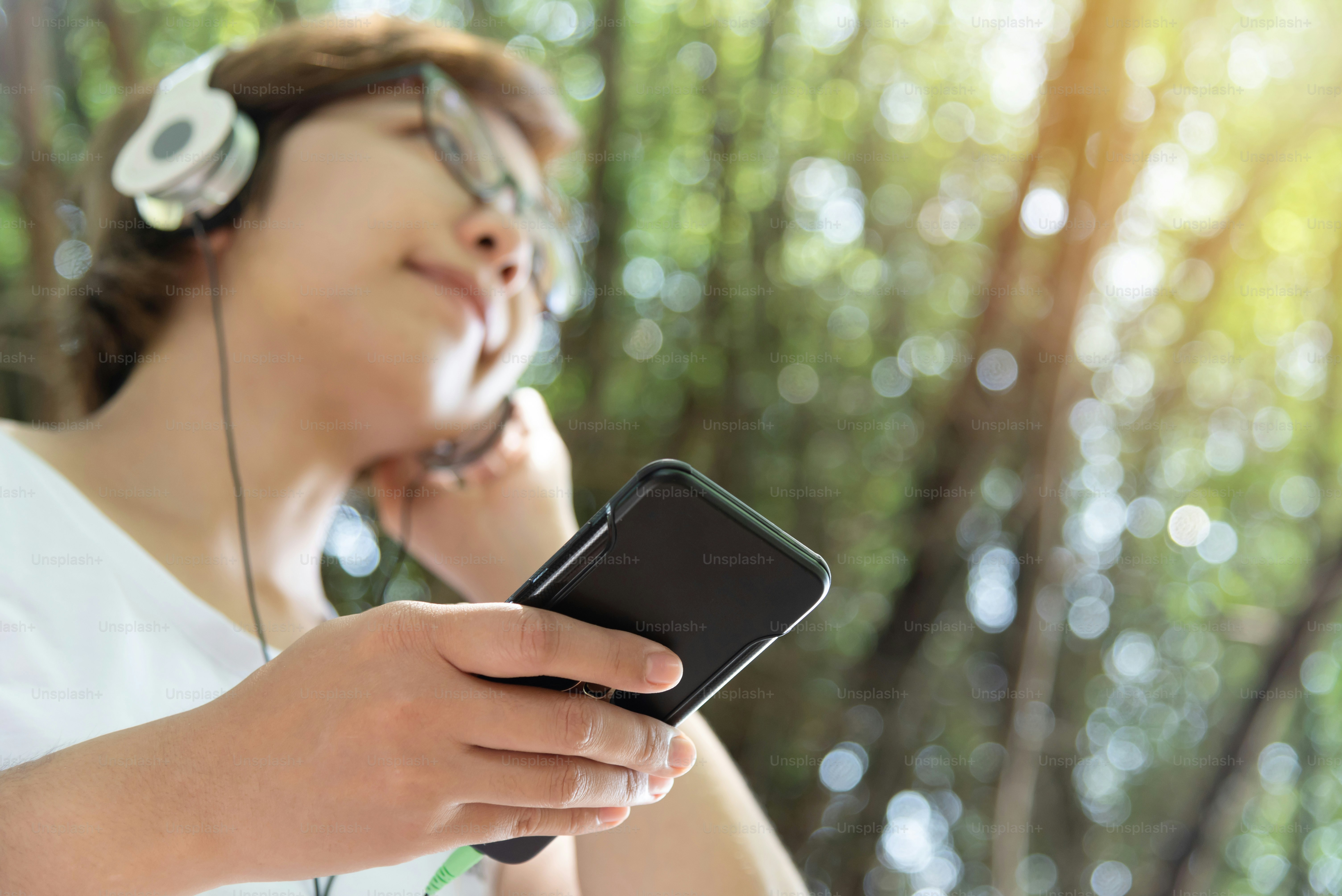 Happy Asian Woman listening to the music with headphone and smart phone at outdoor. Having fun. Relaxed.