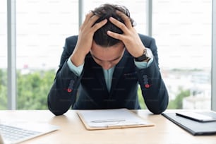 Un hombre de negocios estresado se sostiene la cabeza con las manos mientras trabaja en la oficina.