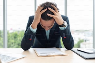 Stressed Businessman is holding his head with his hands while working at the office.