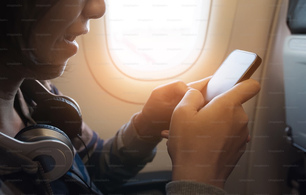 Felicidad de una chica asiática con auriculares usando un teléfono inteligente y sonriendo en el avión.