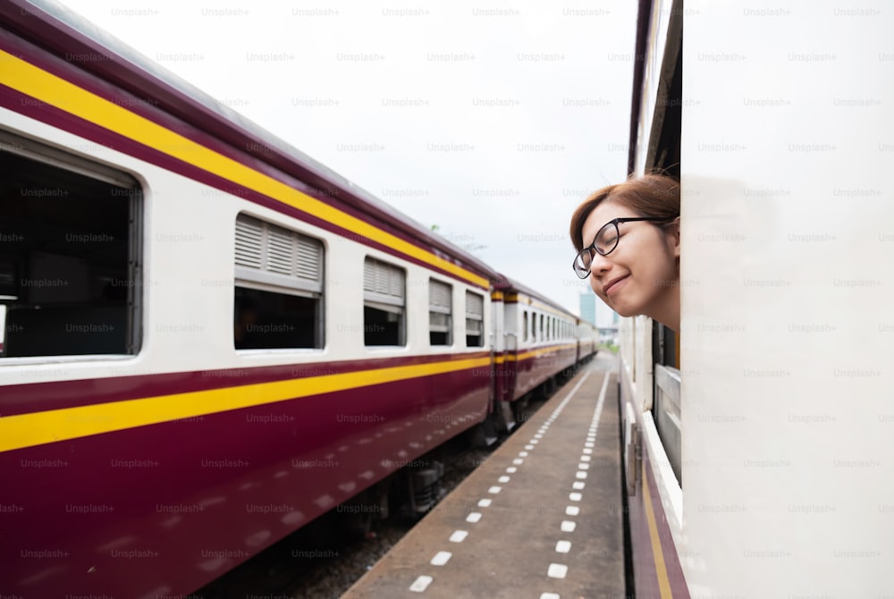 Relaxed Asian female traveler wear glasses breathing fresh air at outside of the train. Smiling face. Travel Concept.