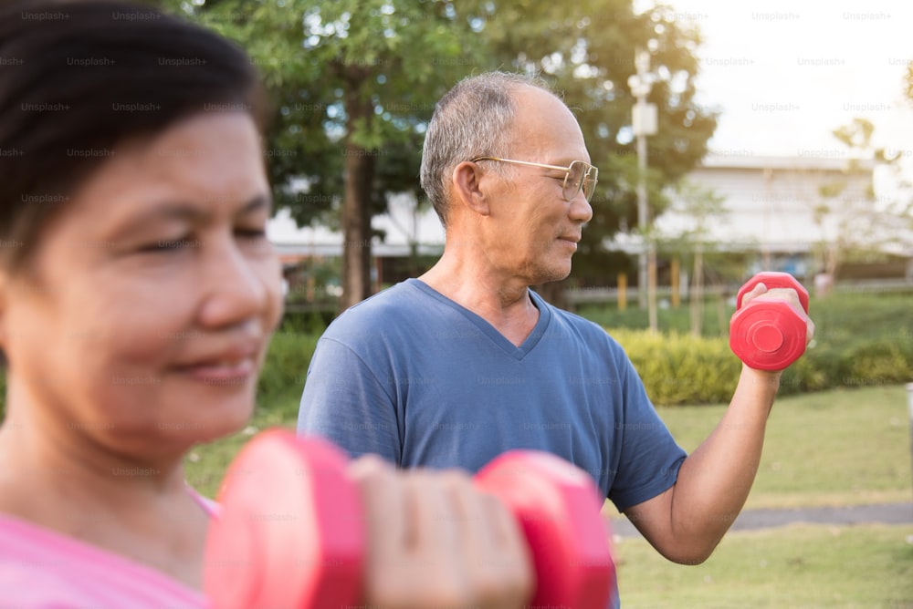 Happy Asian Senior couple exercising with lifting dumbbell at park outdoor together.