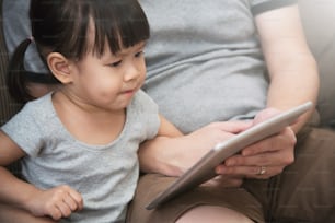 Menina asiática e seu pai sentados e usando tablet digital juntos. Conceito de Conhecimento e Aprendizagem.