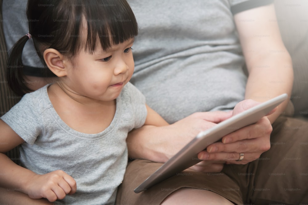 Niña asiática y su padre sentados y usando una tableta digital juntos. Concepto de conocimiento y aprendizaje.