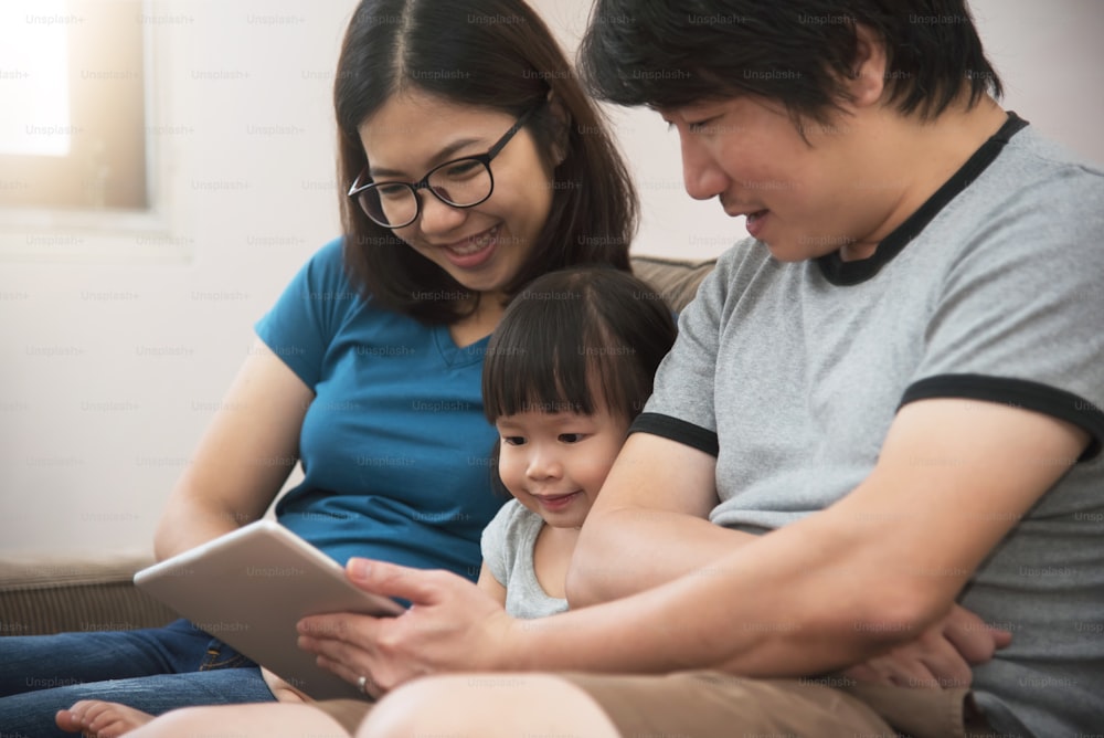 Happiness of Asian  family sitting and playing digital tablet together with technology. Smiling of Young father and mother with little kid girl. Knowledge and Learning concept.