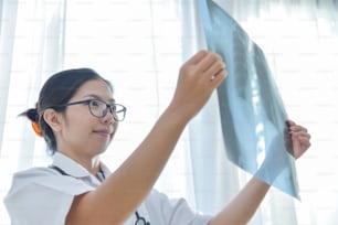 Giovane medico asiatico indossa occhiali che guardano la pellicola a raggi X del paziente.
