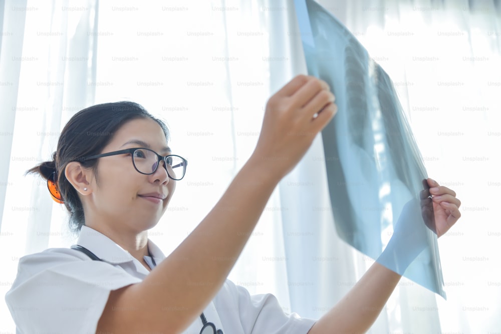 Una joven doctora asiática usa anteojos que miran la película de rayos X del paciente.