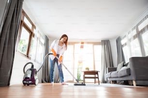 Attraktive asiatische Frau in weißem Hemd benutzt Staubsauger auf dem Teppich oder Teppich und Boden. Reinigung des Hauses.