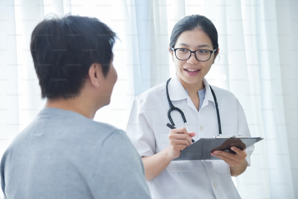 Asian Female Doctor examining and taking note on checklist paper with male patients in medical room.