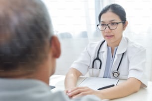 Young Asian Female doctor comforting senior male patient with holding hands in medical office.