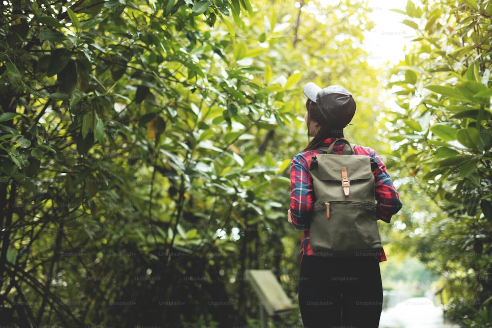 Asian girl traveler in red plaid shirt with backpack walking in the forest. Rear view. Trekking.