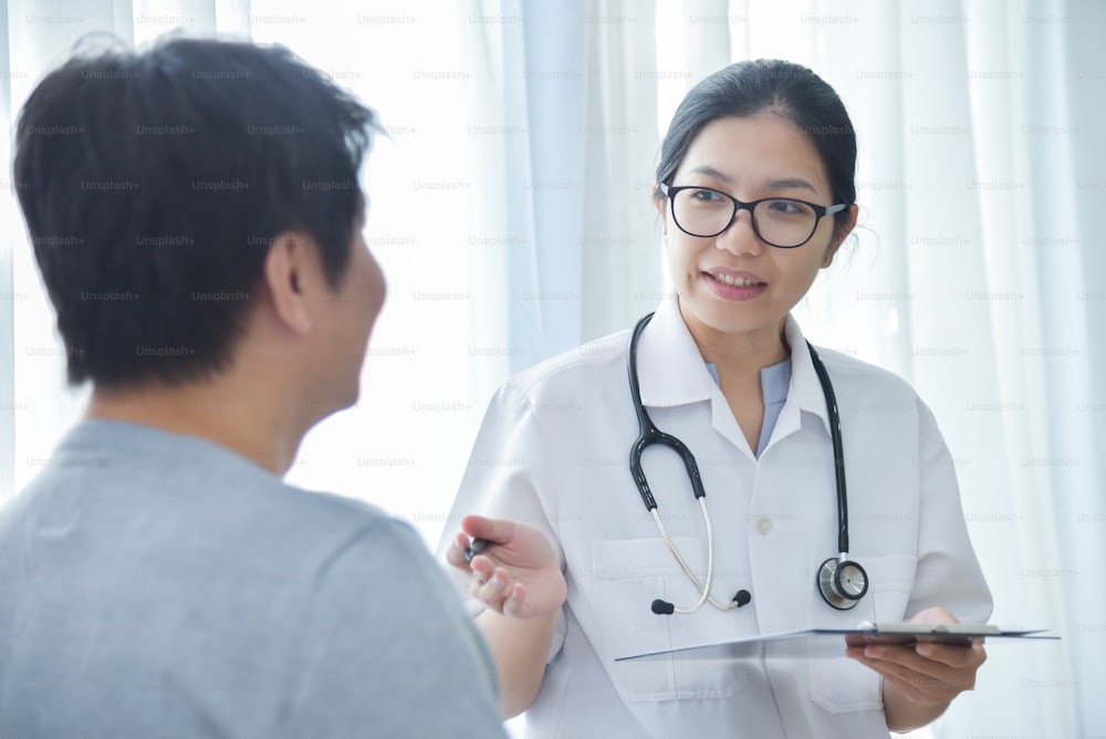 Asiatische Ärztin untersucht und notiert Checklistenpapier mit männlichen Patienten im medizinischen Raum.