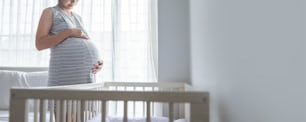 Alegre muchacha asiática embarazada de pie tocando su vientre en el dormitorio, joven esperando mujer disfrutando de la maternidad futura, panorámico, panorámico.