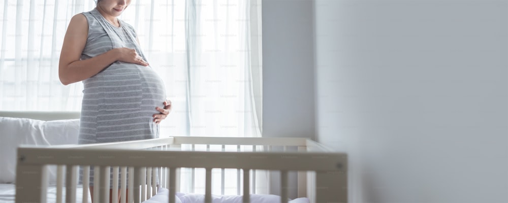 Cheerful pregnant Asian girl standing touching her belly in bedroom, Young expecting Female enjoying future motherhood, Banner, Panoramic.