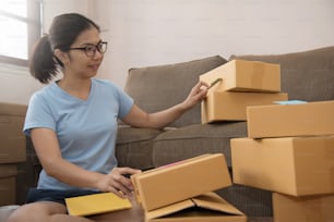 Young Asian woman  checking cardboard boxes in her small warehouse. Own business