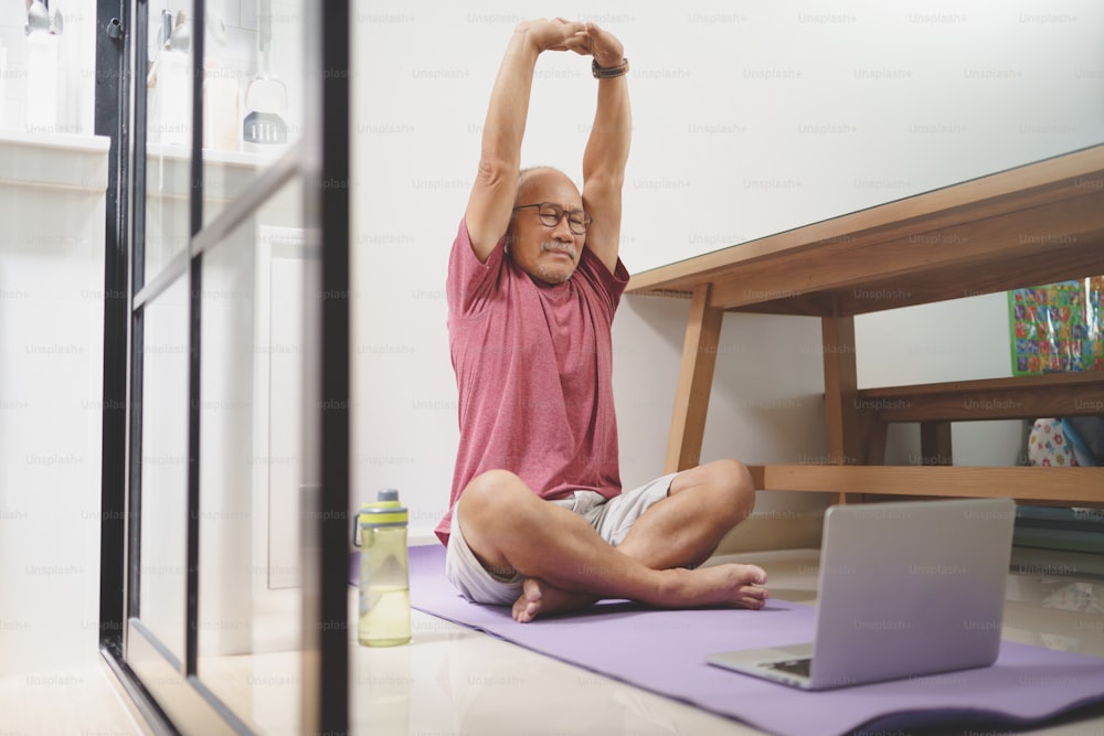 Asian Senior man stretching his arms before yoga exercise online at home.