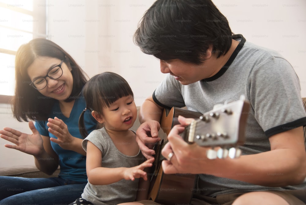 Glückliche Familie. Asiatischer junger Vater, Mutter und Tochter spielen zusammen Gitarre.