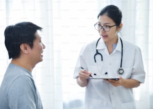 Asian Female Doctor examining and taking note on checklist paper with male patients in medical room.