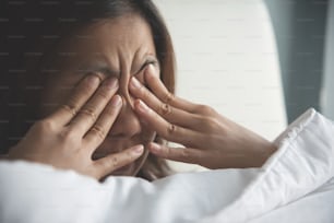 Asian woman rubbing eyes with her hands on her bed. Copy space.