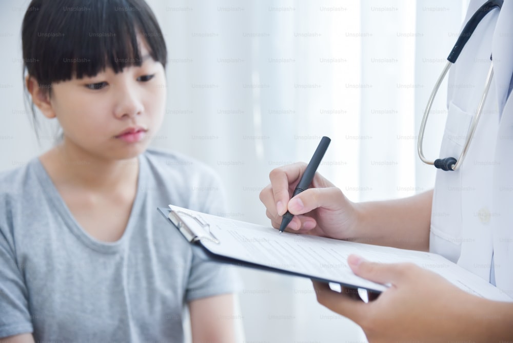 Doctora asiática tomando nota en papel de lista de verificación para una niña pequeña pacientes.